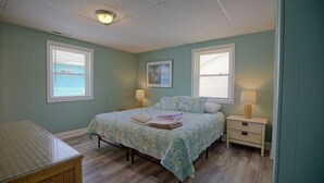 A bedroom with a bed, two bedside tables, a nightstand, a window, and a ceiling light. - Fins Up Unit #2 - On The Bayside - Downtown - Spacious Unit! (Ocean City)