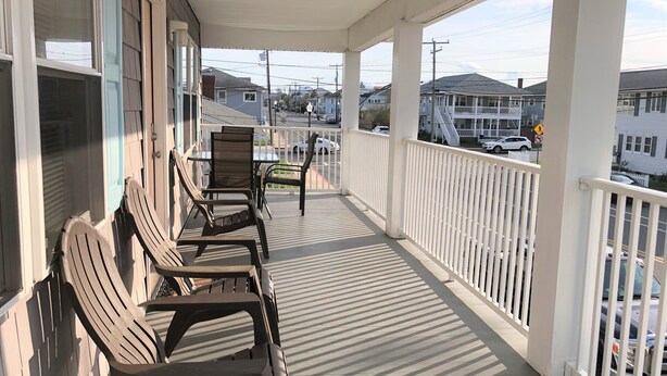 A covered porch with wooden chairs and a table, overlooking a street with buildings and parked cars. - Fins Up Unit #2 - On The Bayside - Downtown - Spacious Unit! (Ocean City)