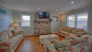 A living room with a stone fireplace, two floral sofas, a coffee table, and a flat-screen TV mounted above the fireplace. - Fins Up Unit #2 - On The Bayside - Downtown - Spacious Unit! (Ocean City)