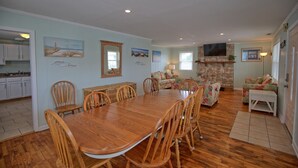 A spacious dining area with a wooden table and chairs, a stone fireplace, and a living room with a sofa and a television. - Fins Up Unit #2 - On The Bayside - Downtown - Spacious Unit! (Ocean City)