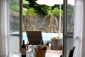 A room with a glass table, a wicker chair, a wicker side table, a bottle of wine, and a fruit basket. - Pool Villa Sesoko jima (Motobu)
