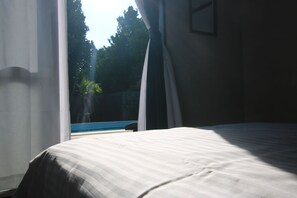 Relax in a serene space with a large bed and a view of the outdoor pool and lush gardens.