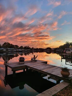 A wooden dock with two Adirondack chairs, a potted plant, and a calm body of water reflecting the sky. - Beautiful waterfront pool home 5 minutes from downtown St Pete! (St. Petersburg)