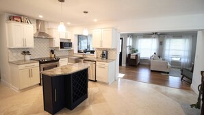 A modern kitchen with white cabinets, a central island, and a dining area with a sofa and a coffee table. - Beautiful waterfront pool home 5 minutes from downtown St Pete! (St. Petersburg)