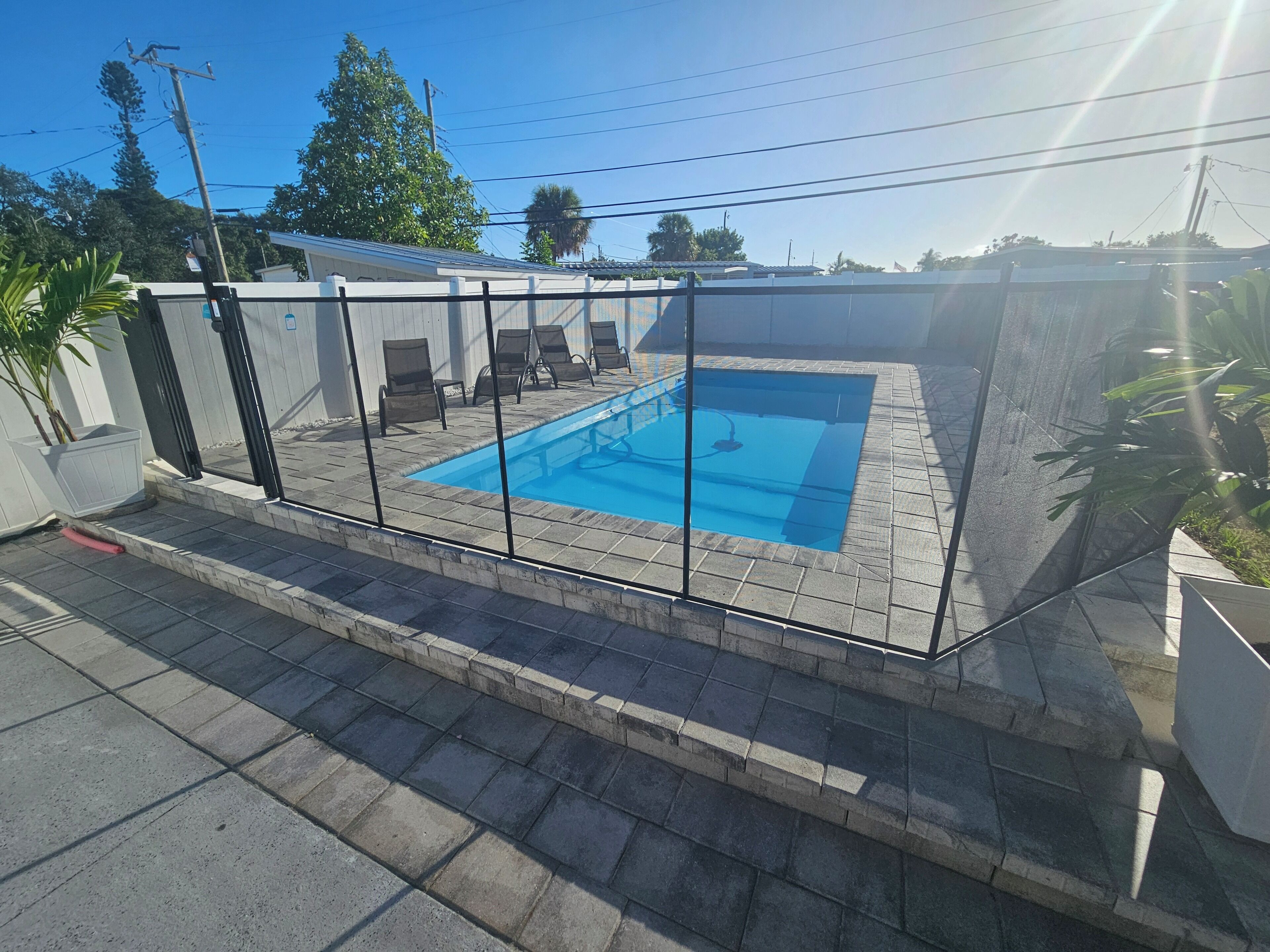 Una piscina rectangular con un borde empedrado y una valla de metal.