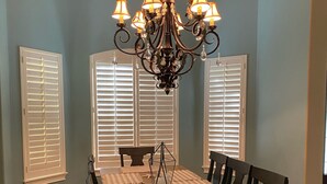 A dining room with a long table, six chairs, a chandelier, and three windows with blinds. - Entire private house VR24-00064  (Sarasota)
