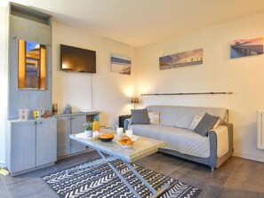 En moderne stue med en grå sofa, et spisebord med morgenmadsretter, et fjernsyn ophængt på væggen og kunst på væggene.