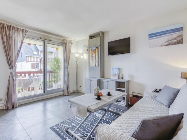 Una sala de estar moderna con un sofá, una mesa de centro y un televisor. Hay una puerta corrediza de vidrio que da a un espacio exterior.