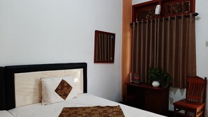 Un lit bien fait, recouvert d’une couvre-lit à motifs, une table de chevet avec un vase et une plante, et une chaise en bois.