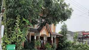 Un hôtel au style architectural traditionnel, doté d’un toit en tuiles et d’un jardin bien entretenu, agrémenté de diverses plantes et d’un grand arbre qui offre de l’ombre.
