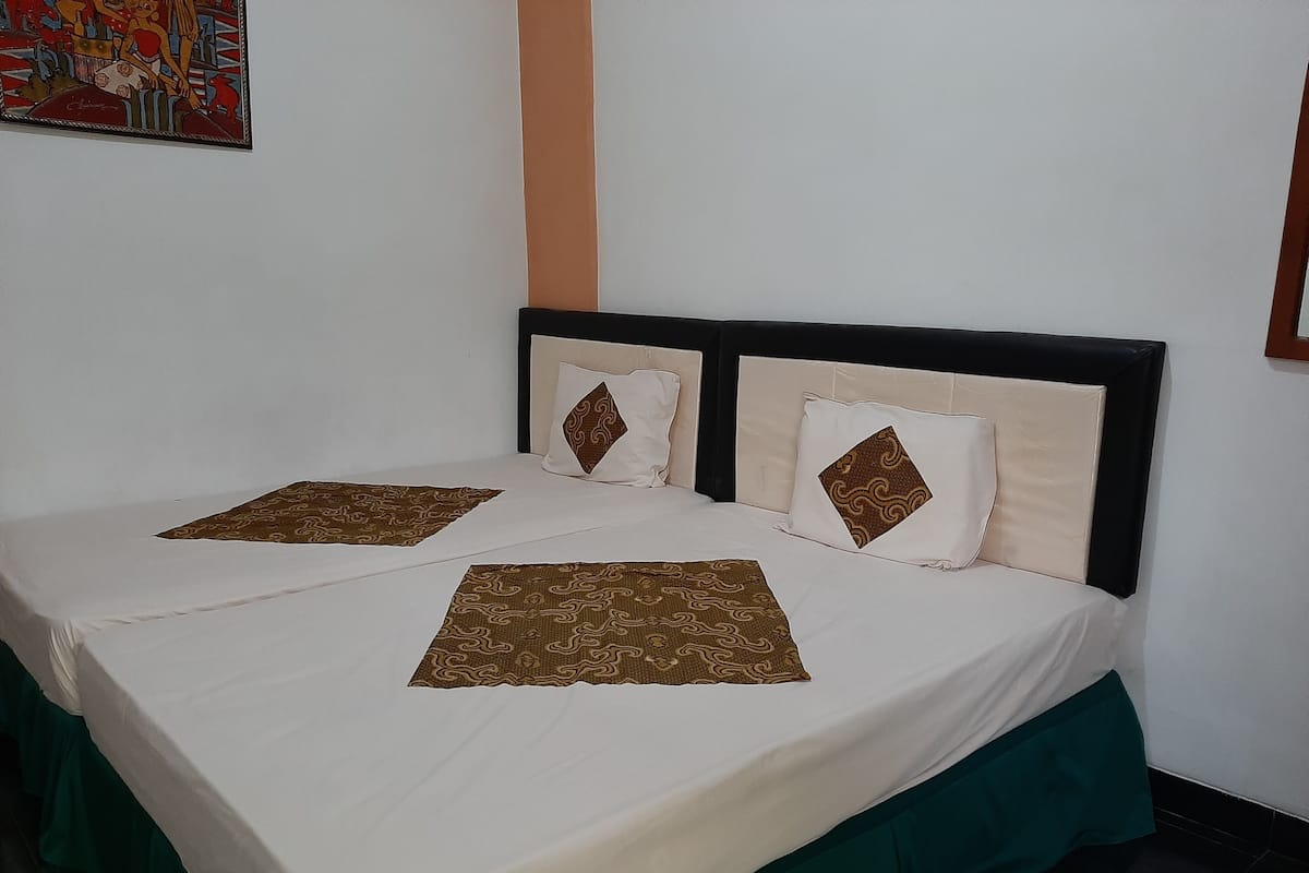 Un lit double avec une couvre-lit blanche et deux coussins décoratifs, une jupe de lit verte et un mur orné d’un tableau encadré.