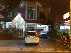 Une voiture blanche est garée devant un immeuble dont l’enseigne lumineuse indique « DANA ».