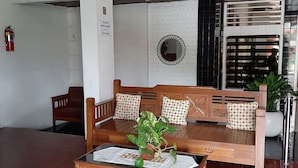 Un canapé en bois avec des coussins à motifs, une petite table avec une plante et un extincteur accroché au mur.