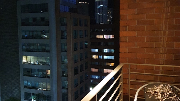 Un balcón con una mesa y sillas de vidrio, con vistas a un paisaje urbano al atardecer.