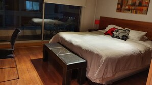 Una habitación de hotel con una cama, un banco, un escritorio y un ventanal grande.