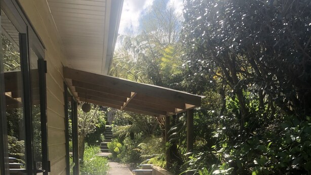 Une terrasse en bois agrémentée d’une pergola, entourée d’une végétation luxuriante et offrant une vue sur le ciel.