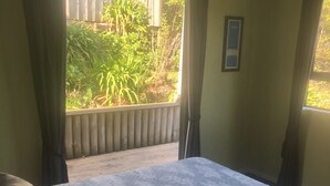 Une chambre à coucher avec un lit, deux oreillers, une fenêtre avec des rideaux et une vue sur la verdure à l’extérieur.