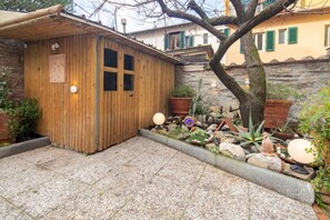 Uma estrutura de madeira com porta e janelas, rodeada por um pátio de brita e plantas em vasos.