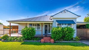 A single-story house with a front porch, a covered entryway, and a small front yard with a lawn and shrubs. - Very comfortable, spacious home. (Cessnock)