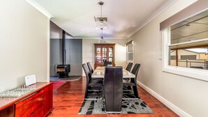 A dining area with a glass-top table, black leather chairs, a wooden cabinet, and a black and gray rug. - Very comfortable, spacious home. (Cessnock)