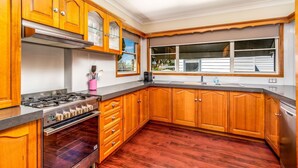 A kitchen with wooden cabinets, a stainless steel stove, and a window with blinds. - Very comfortable, spacious home. (Cessnock)
