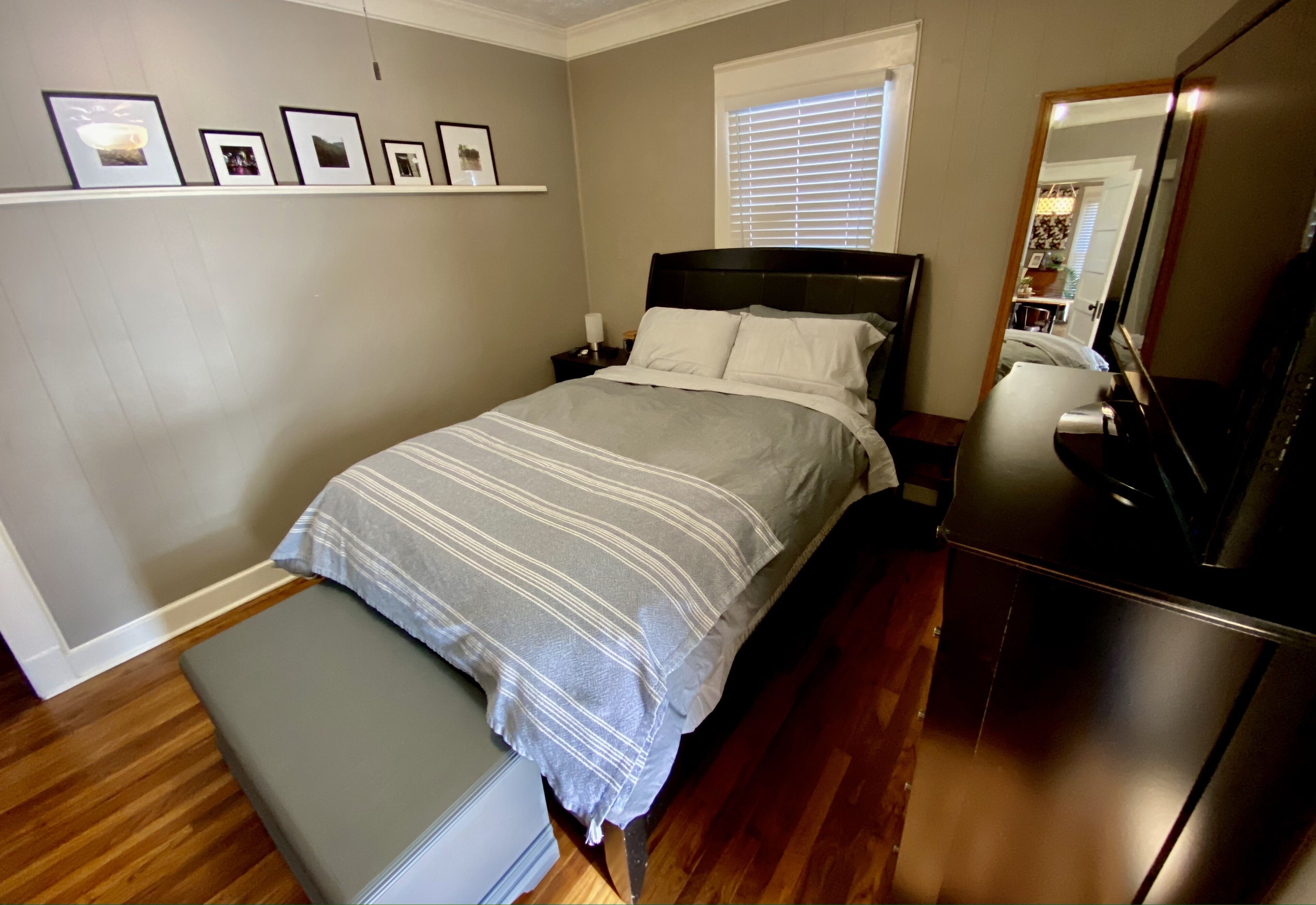 A bedroom with a bed, nightstand, bench, dresser, and a mirror.