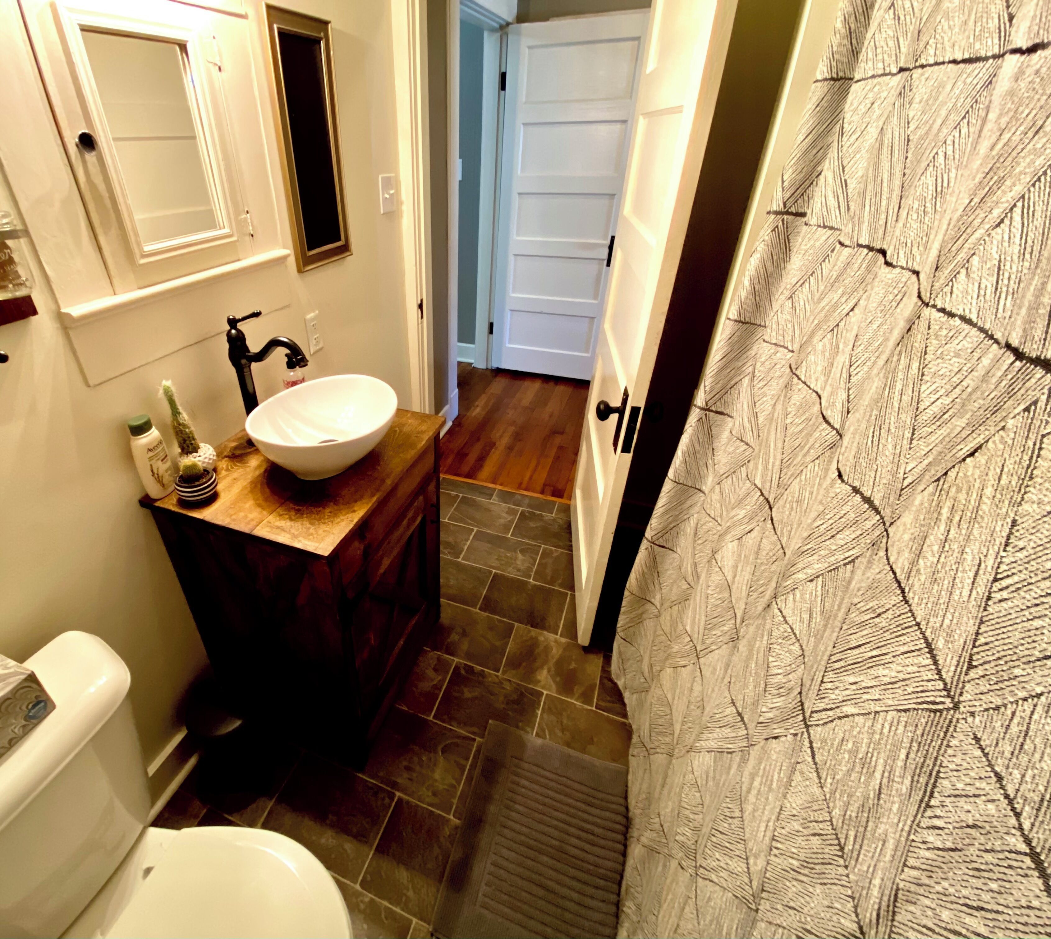 Une salle de bain avec un lavabo blanc, un meuble-lavabo en bois foncé et un espace douche agrémenté d’un rideau à motifs.