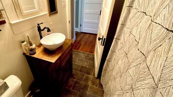 Une salle de bain avec un lavabo blanc, un meuble-lavabo en bois foncé et un espace douche agrémenté d’un rideau à motifs.