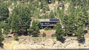 Une maison située sur la côte, dotée d’une grande terrasse et entourée d’une forêt dense de pins et d’un terrain rocheux.