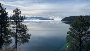 Un lac paisible aux eaux limpides, sous un ciel dégagé, entouré d’arbres et dominé par des montagnes lointaines.