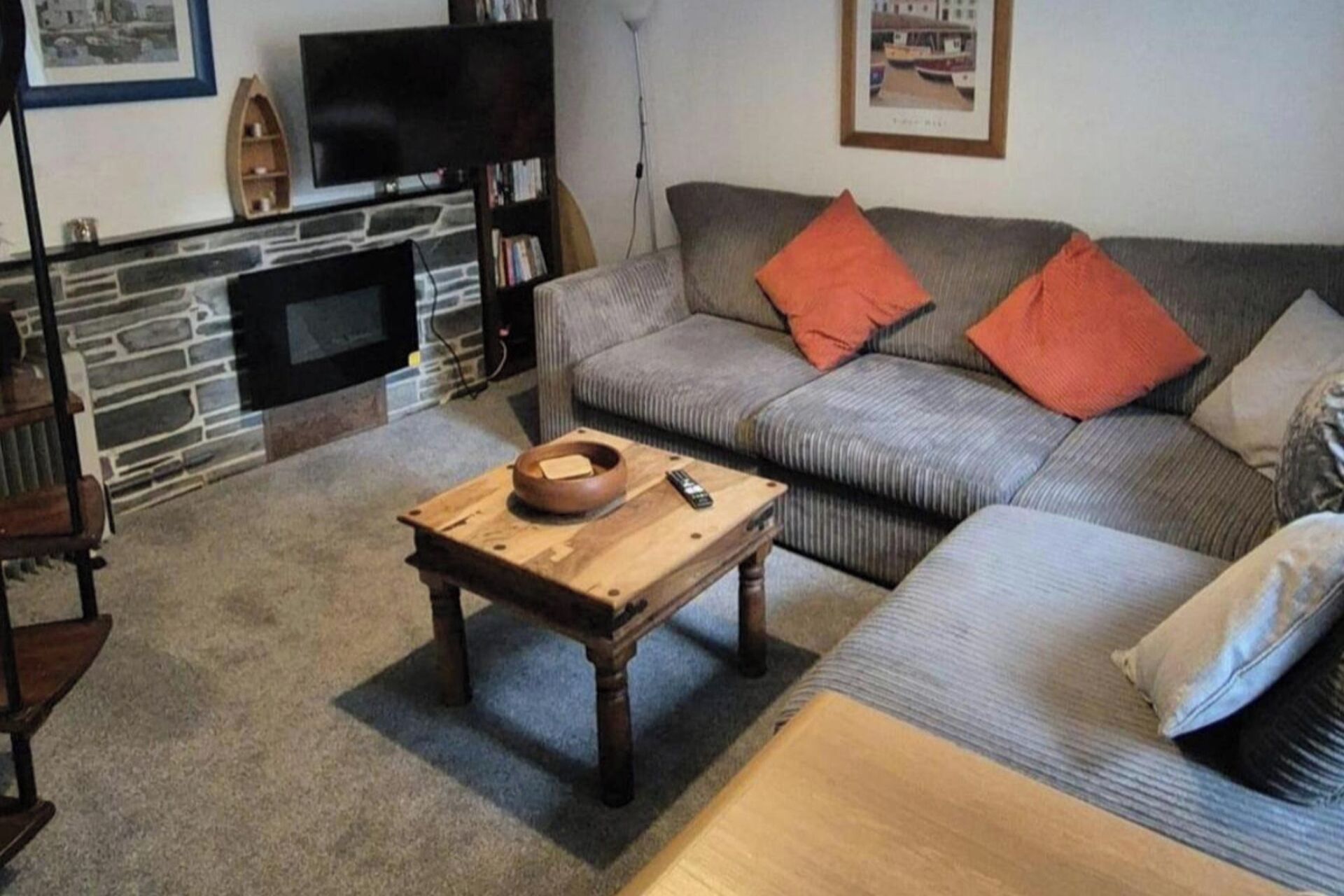 A living room with a stone fireplace, a grey sofa with orange cushions, and a wooden coffee table.