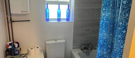 A compact bathroom with a toilet, a window with blue bottles, a radiator, and a shower curtain.