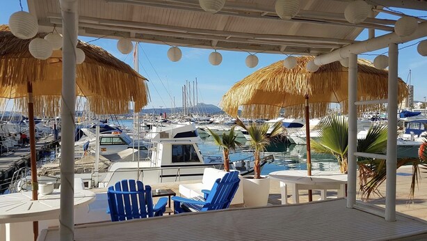 A covered outdoor seating area with thatched umbrellas, a view of a marina with boats, and a table with chairs. - Very beautiful modern 2-Bed Apartment in Javea (Javea)