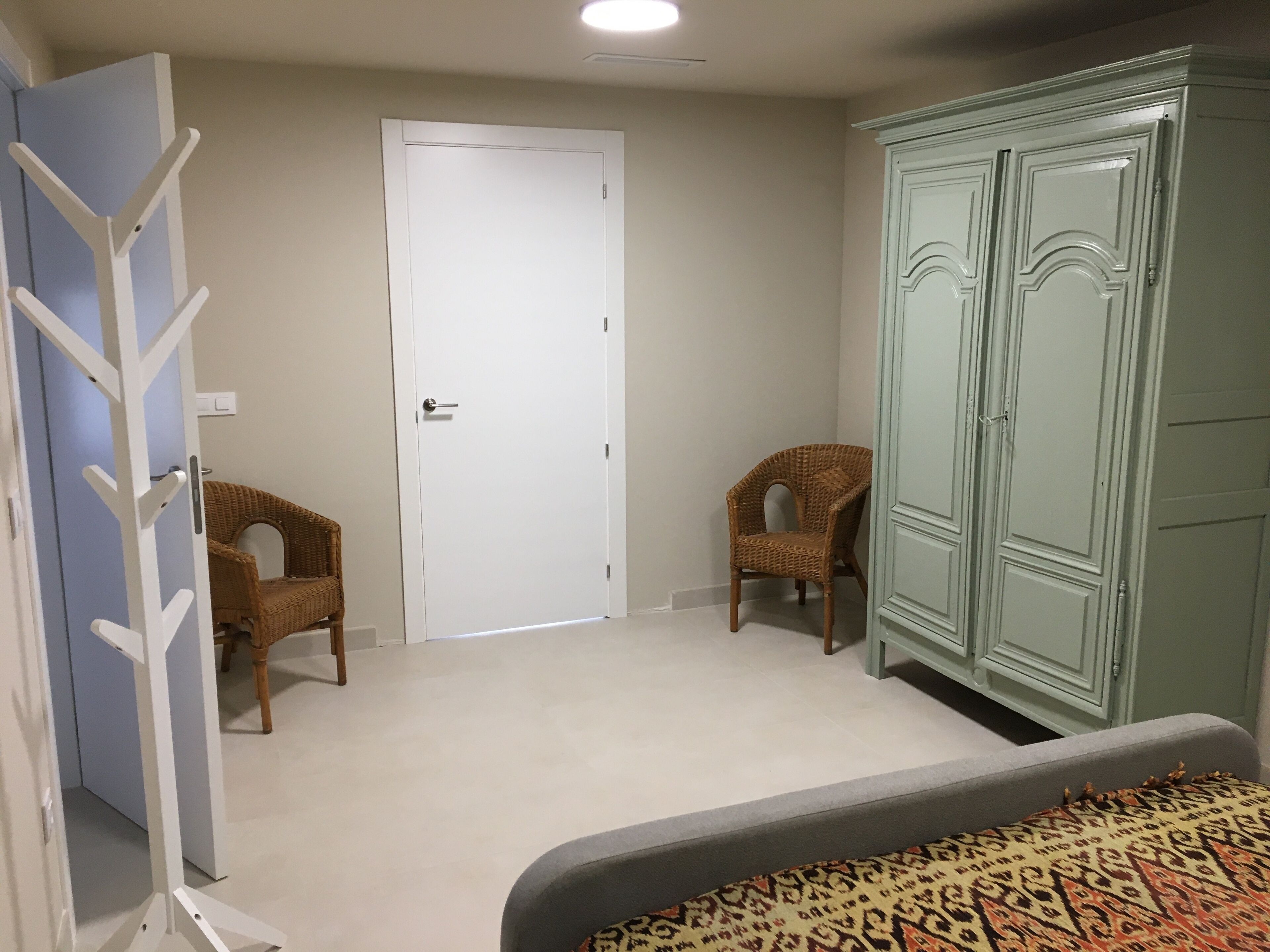 A room with a white door, two wicker chairs, a green wardrobe, and a patterned rug.