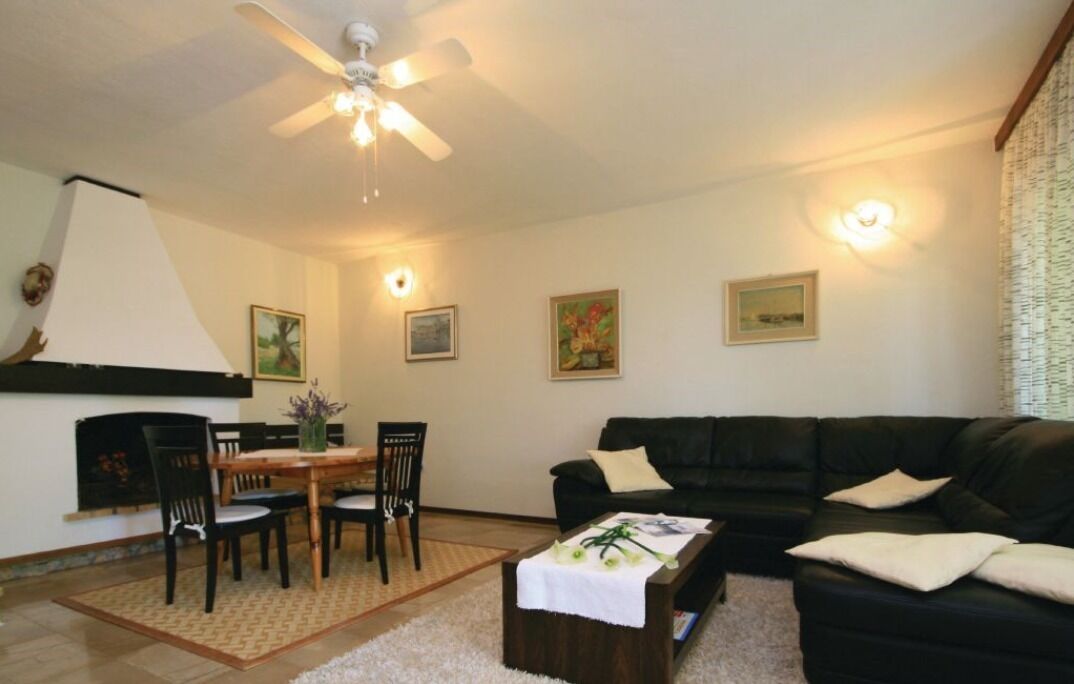 A living room with a black leather sofa, a wooden dining table with chairs, a ceiling fan, and wall-mounted light fixtures.