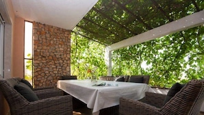 Un espace extérieur aménagé avec des meubles en osier et une table, le tout abrité par une pergola adossée à un mur en pierre.