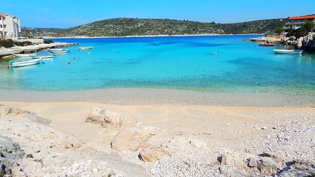 Un paysage côtier avec une eau turquoise cristalline, des bateaux et un terrain rocheux.