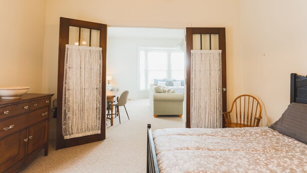 A bedroom with a bed, a wooden dresser, a chair, and a desk with a lamp.