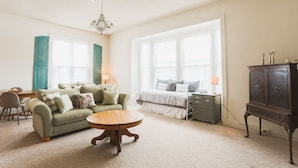A spacious living room with a sofa, a round coffee table, and a bed with a nightstand.