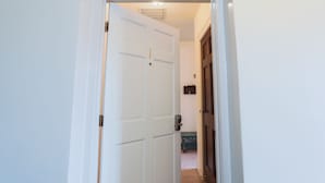 A hallway with a white door, a wooden door, and a small table with a dark-colored object on it.