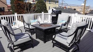 Una terraza con mobiliario exterior, incluyendo sillas, una mesa y una parrilla.