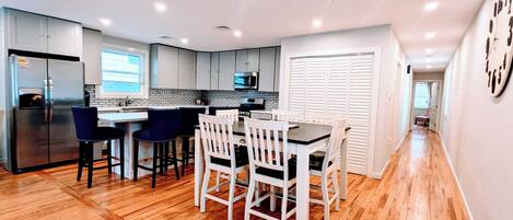 A modern kitchen with a central island, bar stools, and a dining table with chairs.