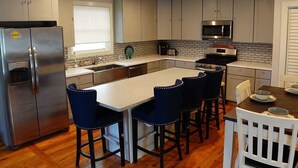 Una cocina moderna con electrodomésticos de acero inoxidable, una isla central con taburetes de bar y una barra desayunadora.