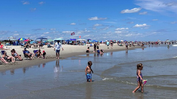 Una playa concurrida donde gente se relaja y niños juegan en el agua.