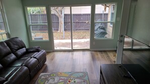 Un salon avec un canapé en cuir foncé, un tapis aux couleurs vives et une porte-fenêtre coulissante donnant sur un jardin.
