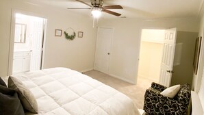 Une chambre à coucher comprenant un lit, un ventilateur de plafond, une porte et un petit coin salon.