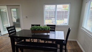 Un espace repas comprenant une table et des chaises en bois, un banc et un bac à fleurs contenant des plantes vertes.