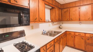 A kitchen with wooden cabinets, a stove, a microwave, and a sink. - Sleeps 4 Fully Equipped Apartment Near Golf Courses (Corry)