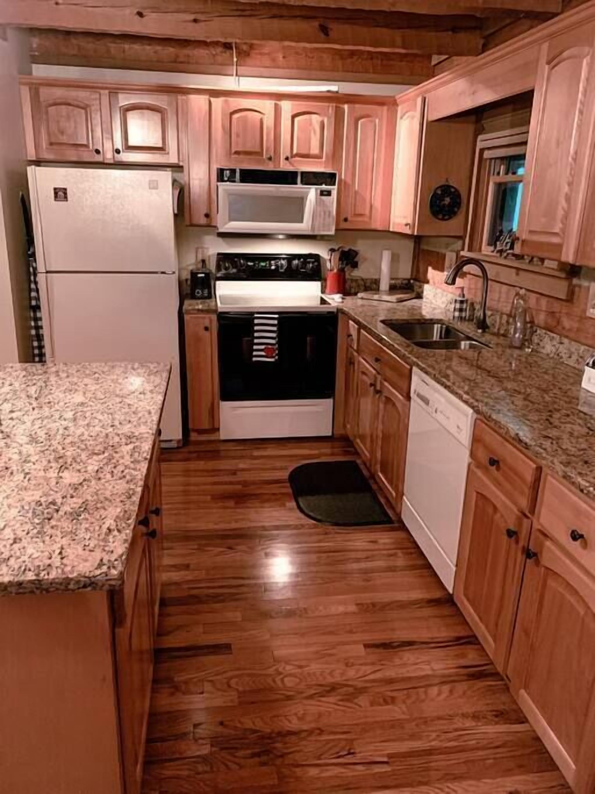 A compact kitchen with wooden cabinets, a refrigerator, a microwave, an oven, and a dishwasher.