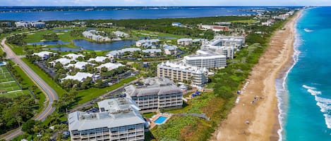 An aerial view of a coastal resort with beachfront properties, a golf course, and a swimming pool.